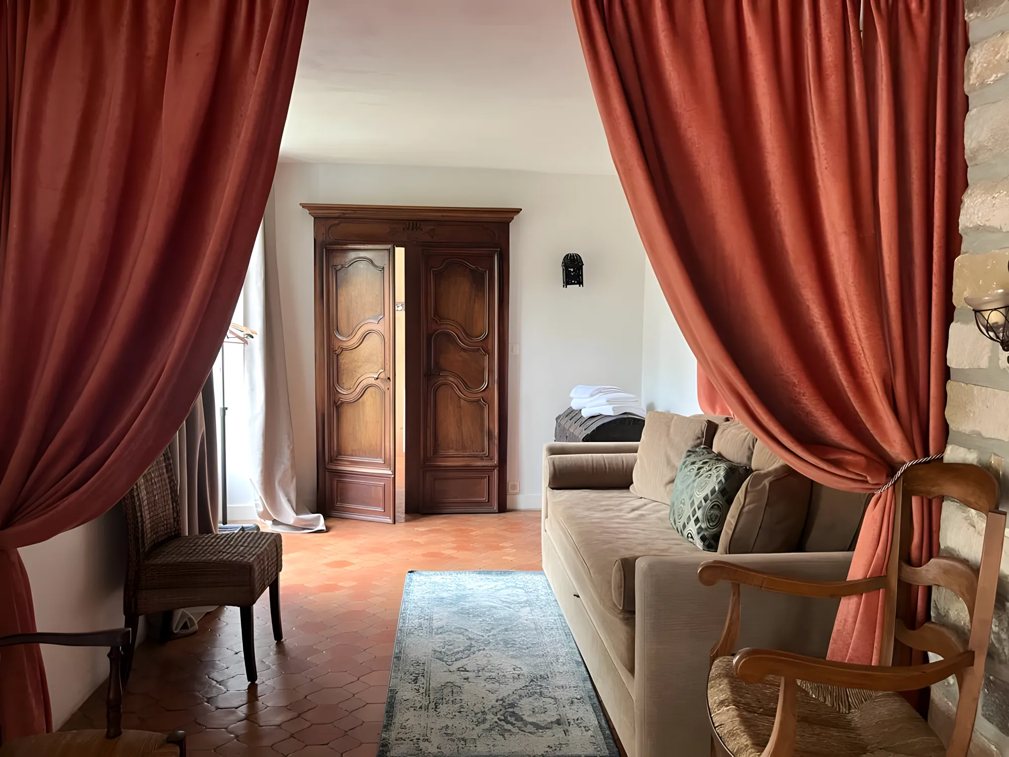 A sitting room of the gîte, rust curtains, a beige sofa and an old armoire
